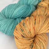 skein of aquamarine yarn with skein of orange yarn with aquamarine speckles